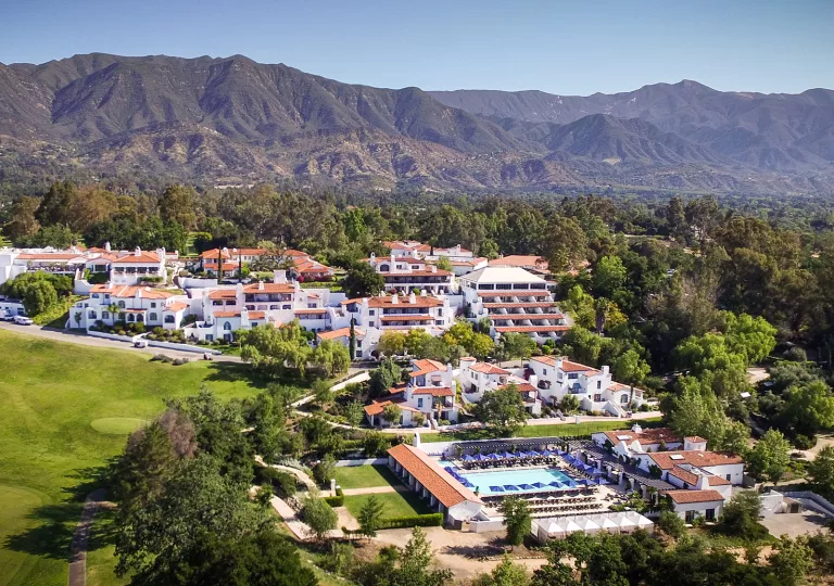 Exterior, sky view of white and brown hotel buildings, with large mountains in the background