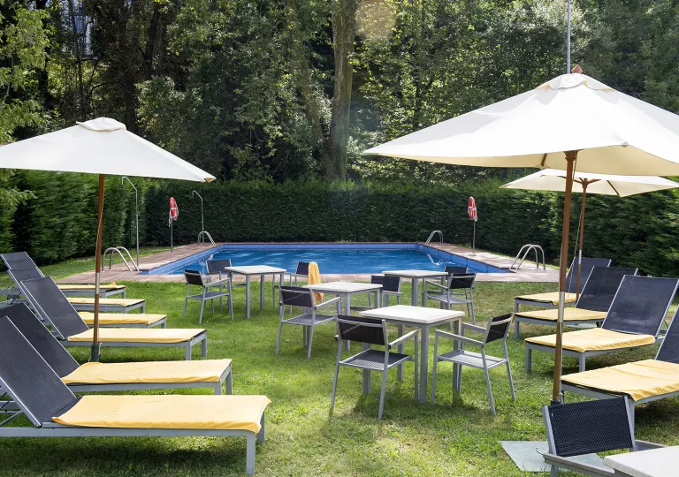 Outdoor pool with reclining chairs and umbrellas on a grass field