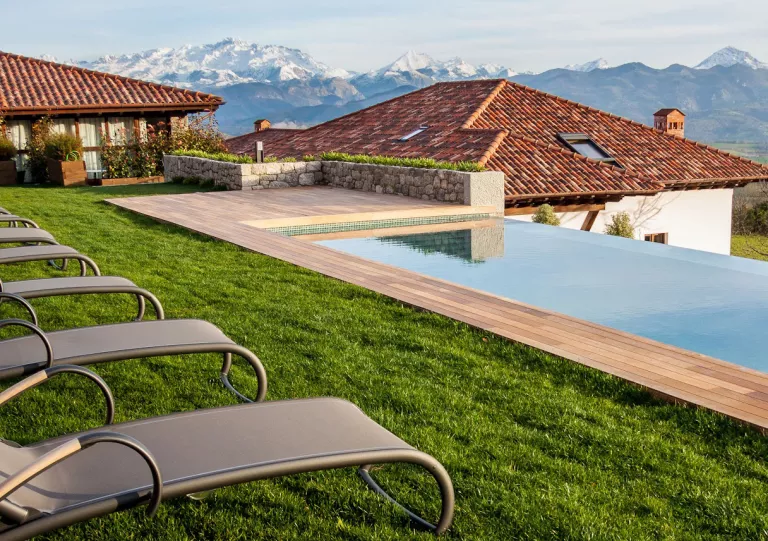 Outdoor pool surrounded by grass, gray reclining chairs and buildings in the background
