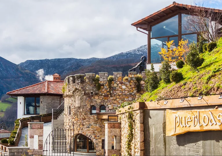 Exterior view of stone buildings, with a staircase on the left and a statue on the top floor