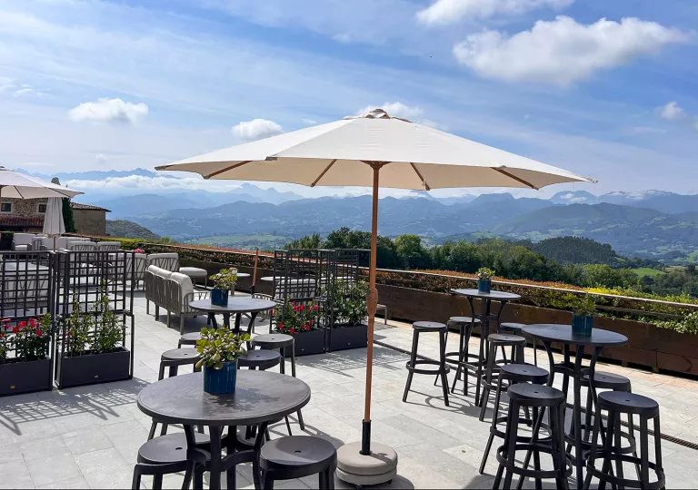 Rooftop patio with black, circular chairs and tables, looking out towards an open valley