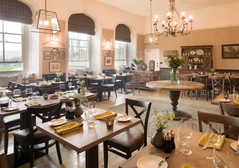 Dining hall with wooden tables and leather chairs, with large windows on the left