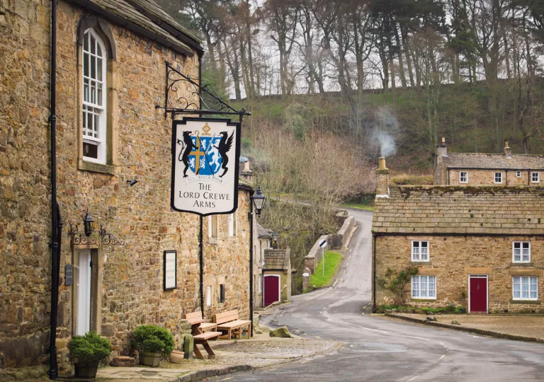 Rustic, stone building with a sign in front, with a forest in the background