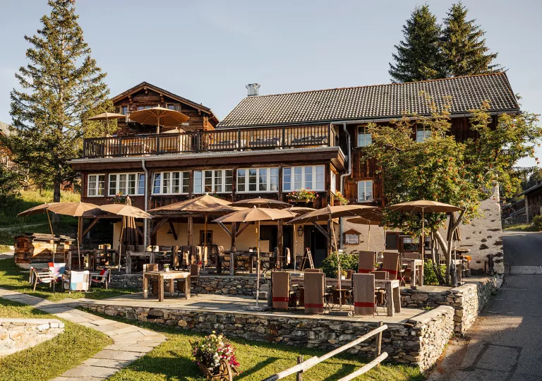 Exterior view of wooden hotel lodge with large umbrellas and dining tables outside