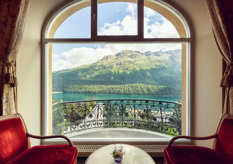 Two red velvet chairs with a large window looking out to a lake and mountains