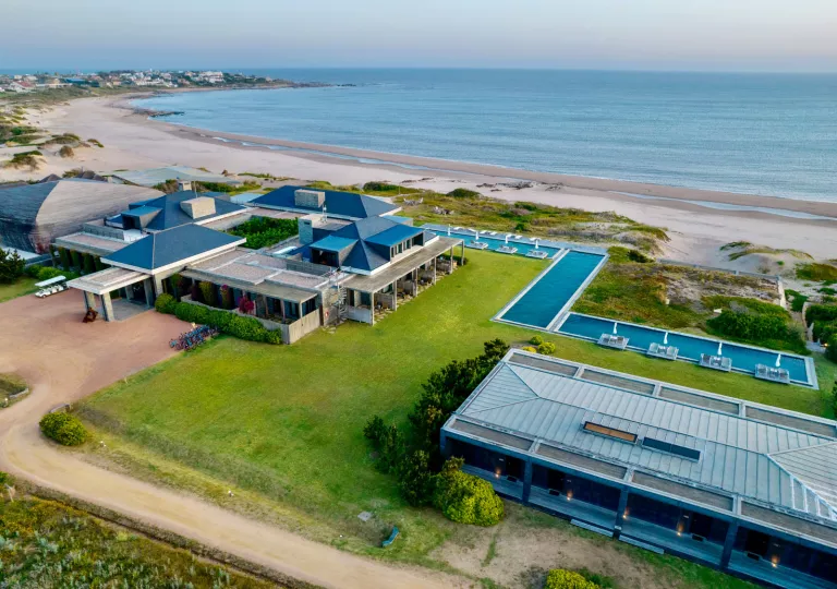 Sky view of two large hotel buildings with a grass field and outdoor pool, with the ocean in the background