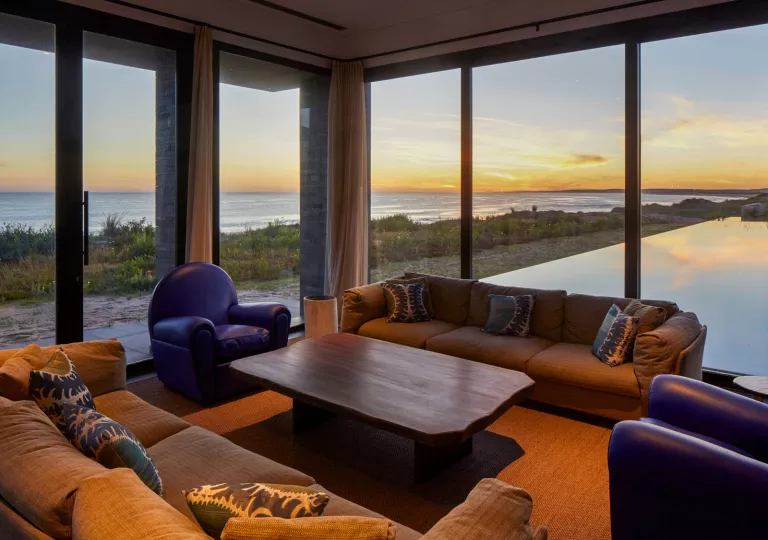 Corner area of a room with large windows, and two couches surrounding a wooden table