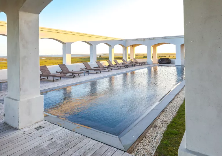 Outdoor pool surrounded by large stone pillars and wooden chairs