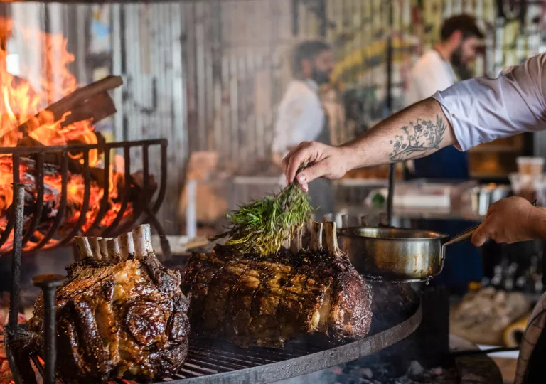 Person sprinkling rosemary on large slabs of meat on a grill
