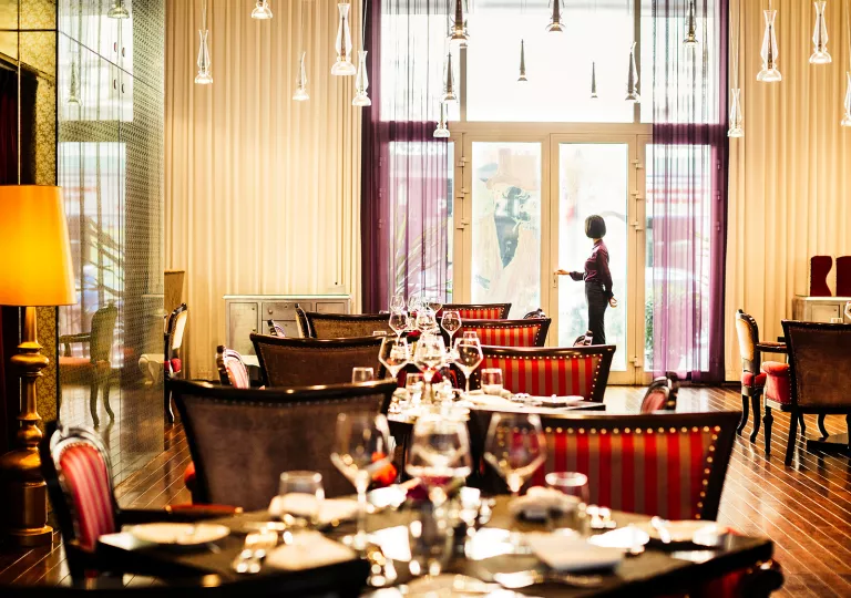 Indoor dining hall with red and tan cushioned chairs, with wine glasses on each table