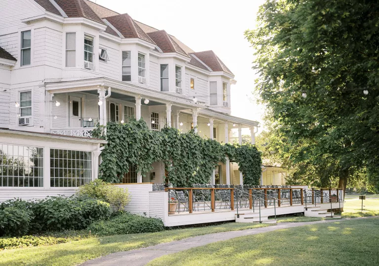 Exterior view of two-story, white house with large bushes and chairs in front