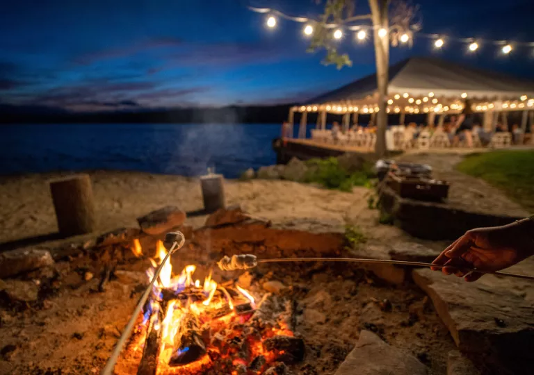 Outdoor firepit by the beach, with people roasting marshmallows on sticks
