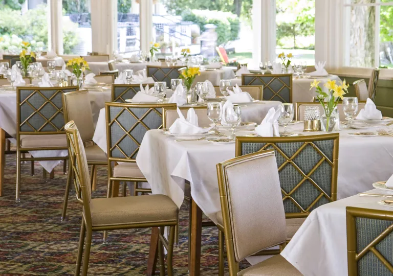 Restaurant dining hall with gold chairs and tables with white cloths on top