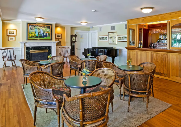 Bar and lounge with wooden chairs around green, circular tables, and a piano in the background