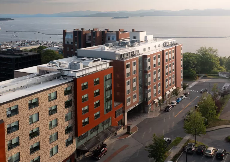 Exterior view of burgundy hotel building with a road in front, and the ocean in the distance