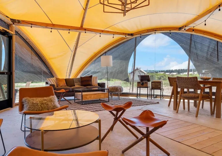 Inside view of a large luxury tent, with couches, cushioned chairs and a dining table