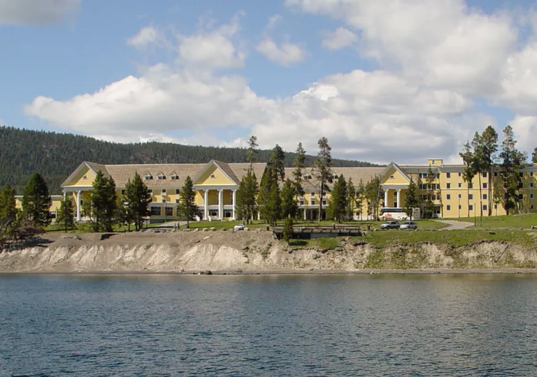 Exterior view of large, yellow building with trees and a lake in front