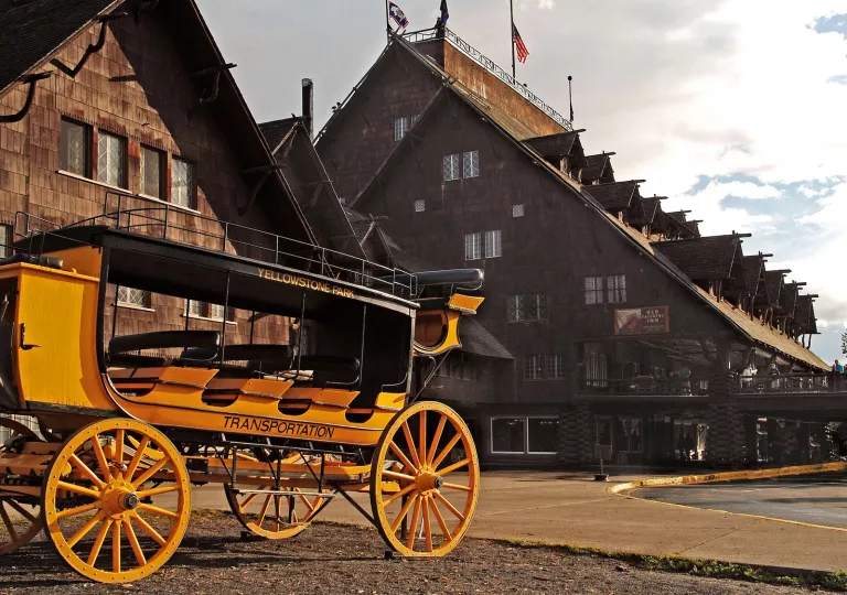 Old-style black and yellow wagon in front of a large, wooden cabin building