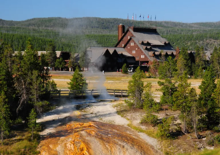 Geyser in the middle of a valley, with a large cabin in the background