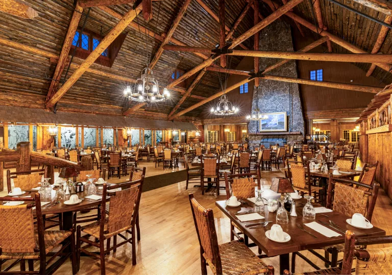 Large cabin dining hall with a large stone fireplace in the background and wooden dining tables throughout the room