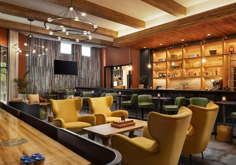 Indoor bar and lounge with yellow and green chairs around wooden tables