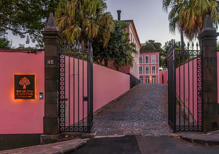 Exterior view of a hotel driveway with pink walls and a black gate