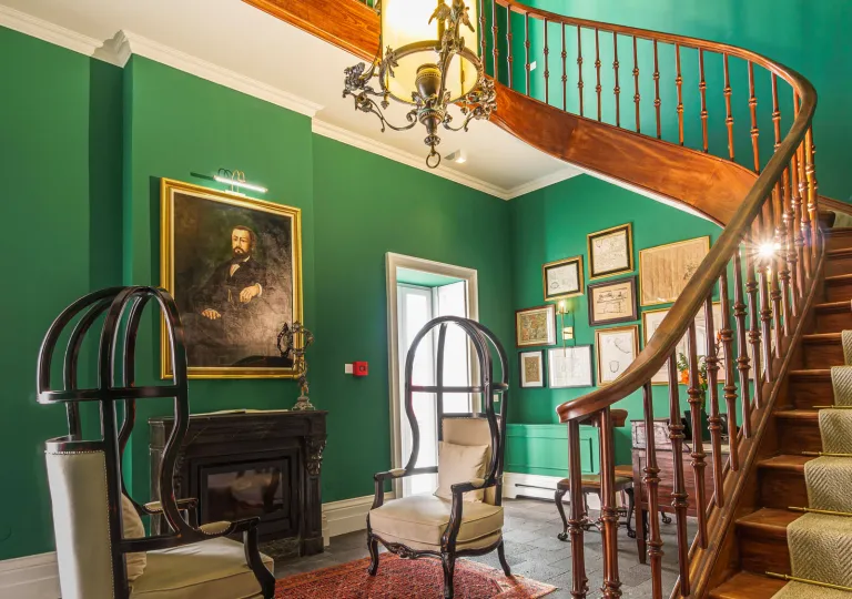 Room with green walls with a wooden staircase and portraits on the walls