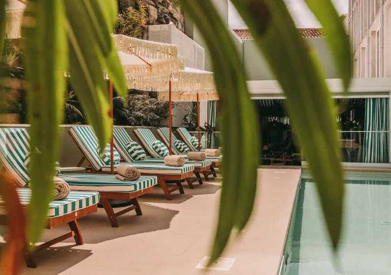Outdoor pool with white and blue striped chairs and white umbrellas