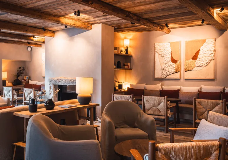 Warm and inviting hotel lounge featuring exposed wood-beam ceilings, upholstered armchairs, woven chairs, and soft ambient lighting. A stone fireplace, textured wall art, and natural materials create a cozy alpine atmosphere at the La Roche hotel in Montenegro..