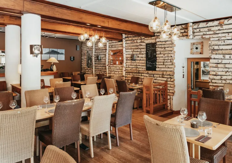 A rustic dining room, featuring birch log walls and modern pendant lighting at Hôtel du Glacier.