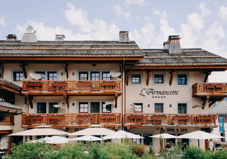 Exterior view of beige and brown hotel building, white beige umbrellas in front