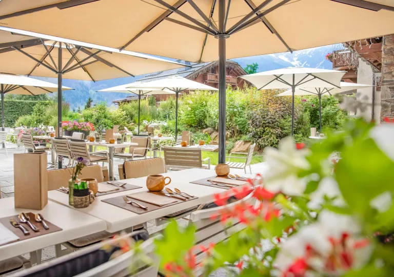 Outdoor patio with long, white dining tables and beige umbrellas