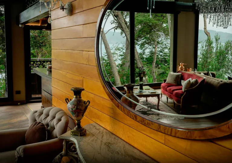 A large round mirror perfectly captures the lakeside sitting area, framed by native Patagonian trees outside at the Calfuco Wine Hotel &amp; Spa in Neuquén, Argentina.
