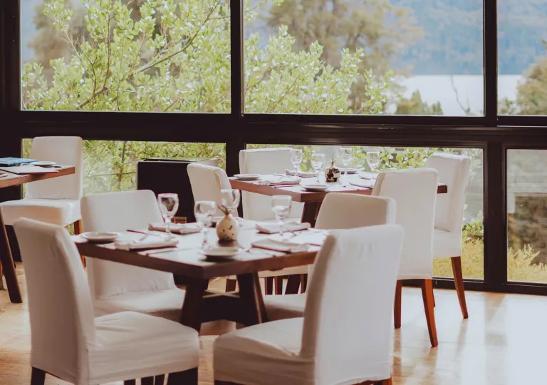 Modern dining room with wood tables and white-covered chairs at Hotel Alto Traful.