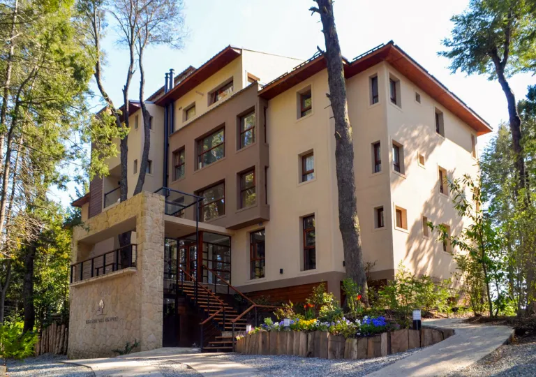 Exterior view of brown and beige hotel building, with tall trees in front