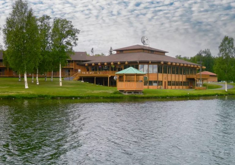 Large cabin-styled building in front of a lake with a grass field
