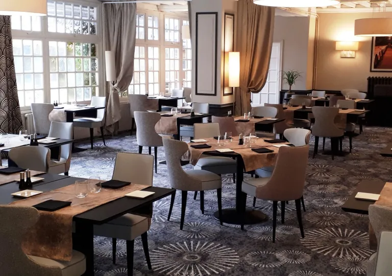 Restaurant dining area with black tables and beige, cushioned chairs, with brown table cloths on each table