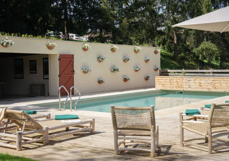 Outdoor pool surrounded by woven chairs and a building with potted plants hanging