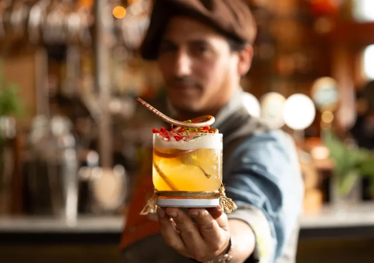 Man holding up a cocktail with a bar in the background