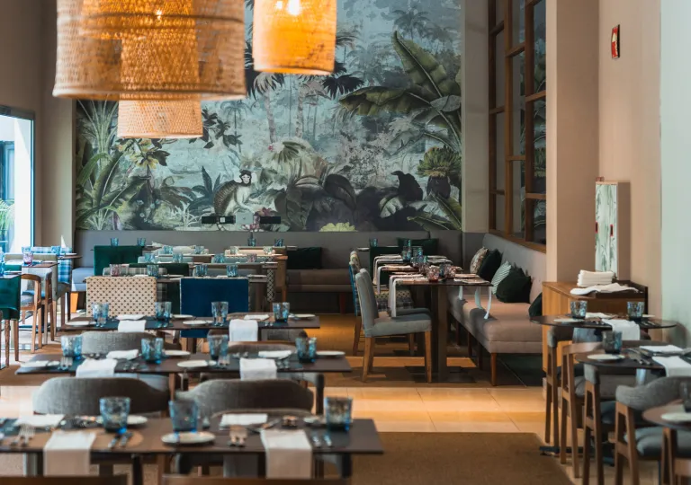 Restaurant with gray tables and dining chairs, with a large painting on the wall