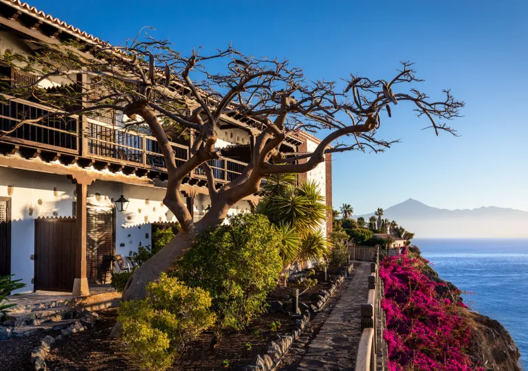 Exterior view of two-story building with a tree in front, and a cliff with the ocean down below