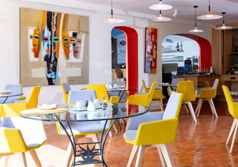 Indoor dining area with glass, circular tables with yellow chairs surrounding
