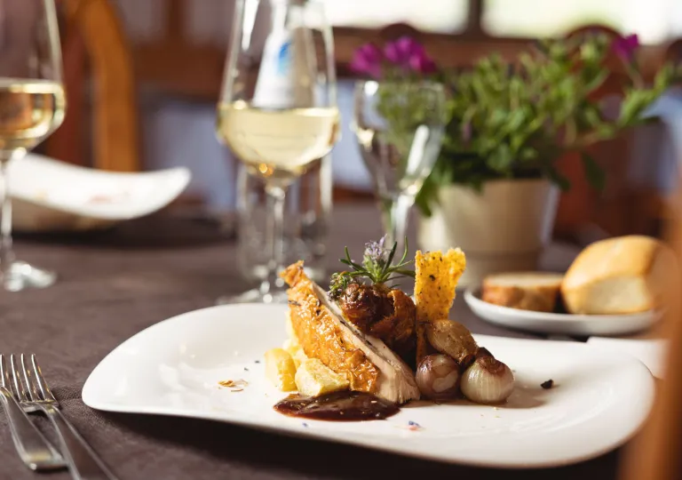 Dining table with a white plate with food an a wine glass in the background