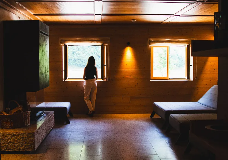 Woman standing in a dimly lit hotel room, looking out an open window