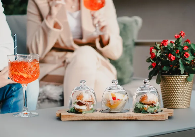 Woman holding a glass, with three little trays of food on the table