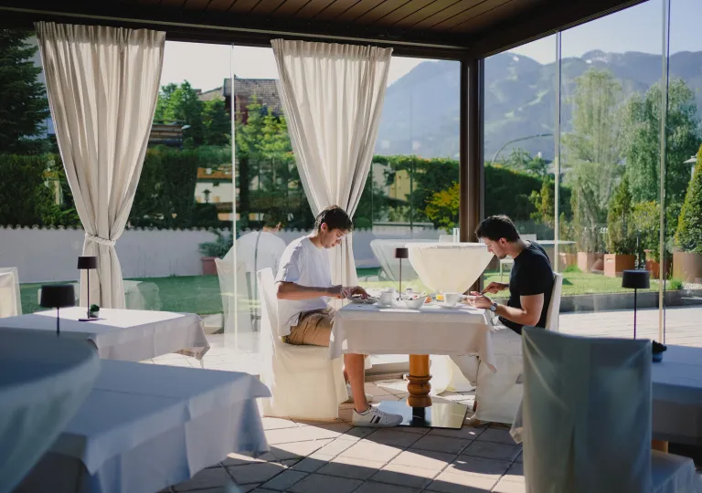 Two men sitting at a white dining table at a restaurant, with large windows along the walls