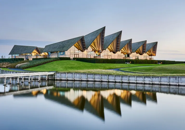 Exterior view of large hotel building with a grass lawn and lake in front