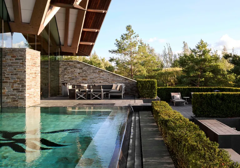 Outdoor pool with trimmed bushes in front and tall trees in the distance