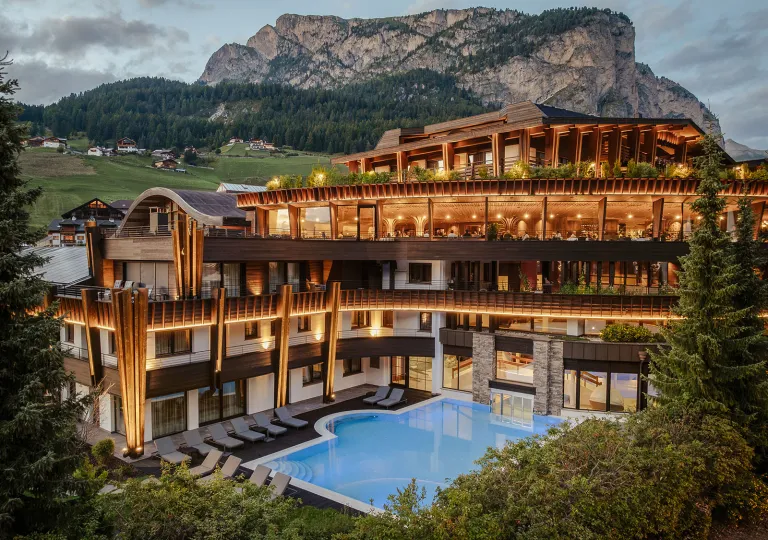 Exterior view of large hotel building with illuminated rooms and an outdoor pool