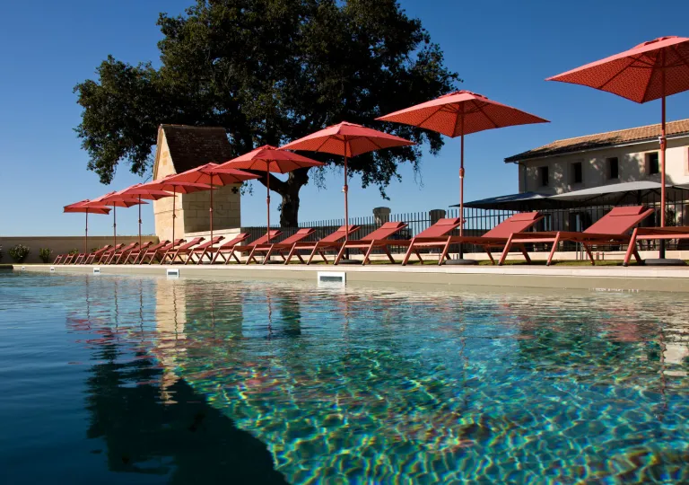 Outdoor pool with a row of red reclining chairs and umbrellas